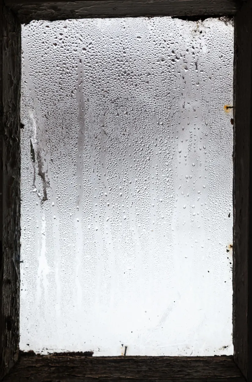 Ein beschlagenes Fenster, an der Scheibe laufen Wassertropfen herunter.