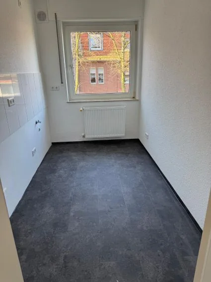 Küche bei der Übergabe: dunkler Boden, weiße Wände, Heizkörper unter dem Fenster.