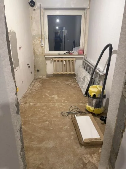 Küche beim Auszug: Estrich offen, Wände geflickt, Staubsauger und Leiter.