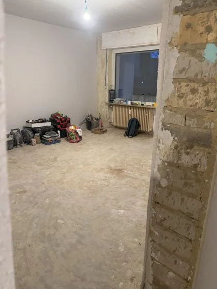 Wohnzimmer beim Auszug: Boden raus, Estrich offen, Werkzeug in der Ecke.